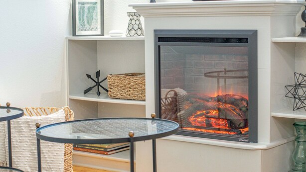 Una chimenea con fuego a la vista, una mesa de vidrio y estantes con objetos decorativos.