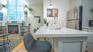 Una cocina moderna con una isla central, un comedor con mesa y sillas, una chimenea y un ventanal con persianas.