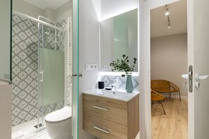 A modern bathroom with a glass shower enclosure, a toilet, a vanity with a mirror, and a wooden cabinet. - Waou Don Quixote Las Letras (Madrid)