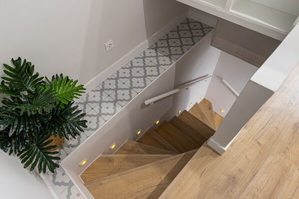 A staircase with a patterned tile wall, wooden steps, and a white handrail.