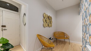 A hallway with two yellow wicker chairs, a white door, and a wall with a geometric patterned wallpaper. - Waou Don Quixote Las Letras (Madrid)