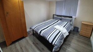 Un dormitorio con una cama, un armario de madera, una ventana con persianas y un pequeño tocador de madera.
