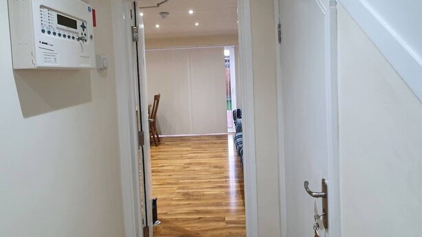Un pasillo con piso de madera, una puerta blanca y un panel eléctrico fijado a la pared.