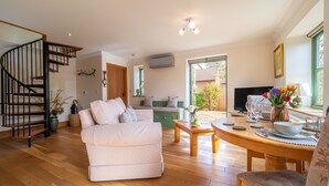 A spacious living room with a staircase, a sofa, a dining table, and a TV.