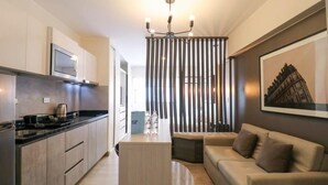 A modern kitchen with a built-in microwave, a coffee machine, and a wooden island. There is a sofa and a small table in the living area, and a framed picture on the wall.