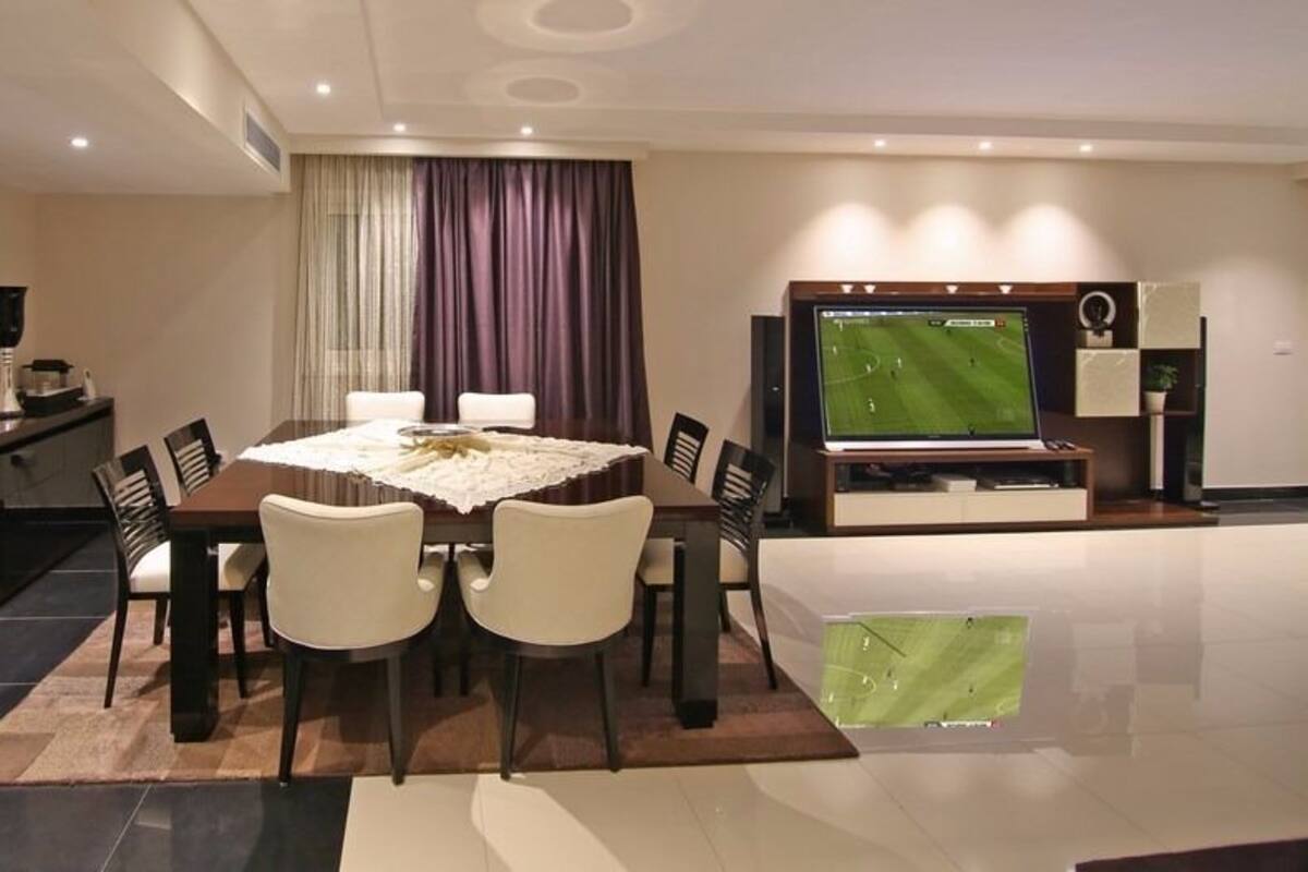 A modern dining area with a round table, chairs, and a television screen displaying a sports game.