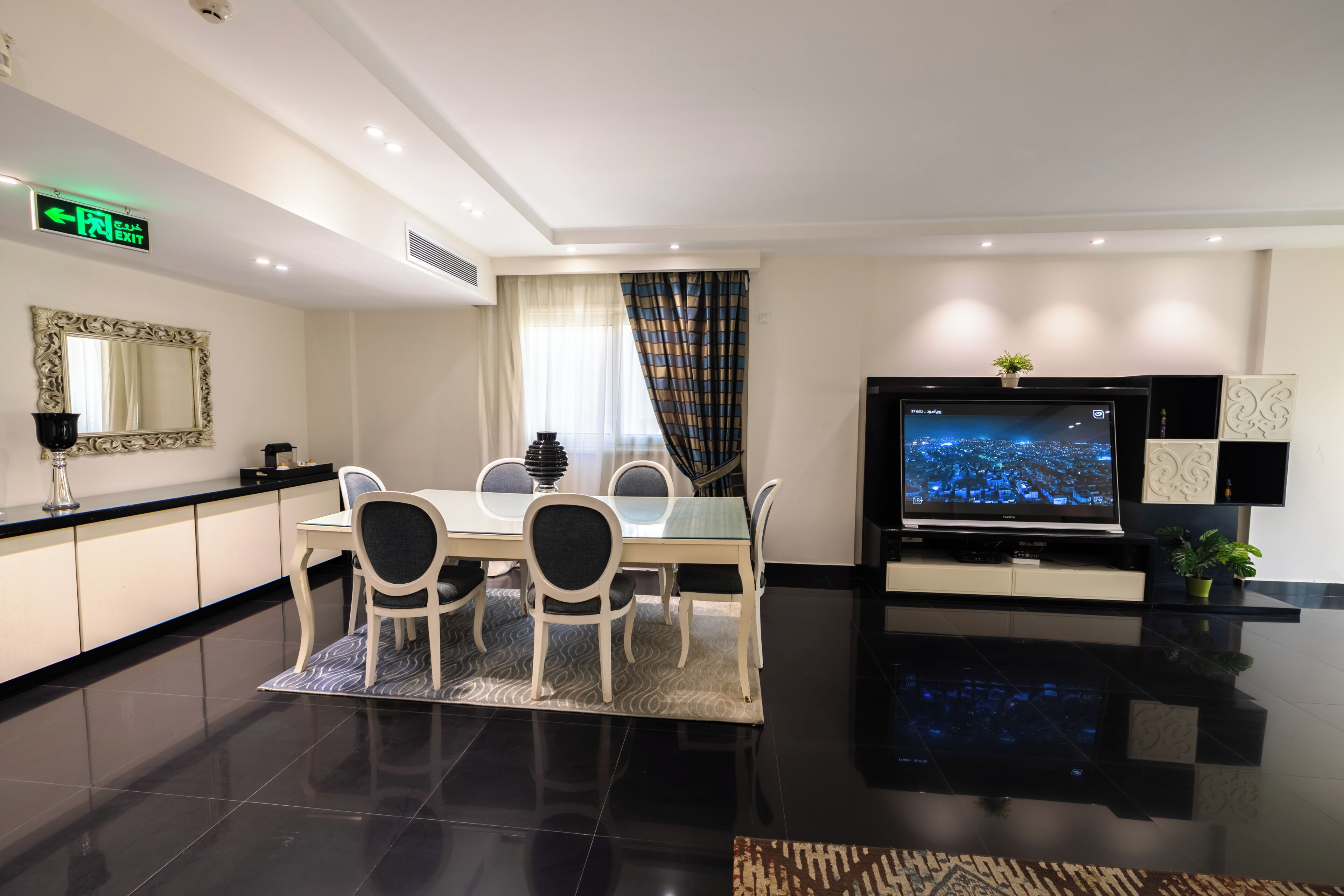 A modern hotel room with a dining area, a flat-screen TV, and a large mirror.