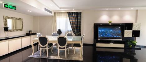 A modern hotel room with a dining area, a flat-screen TV, and a large mirror.