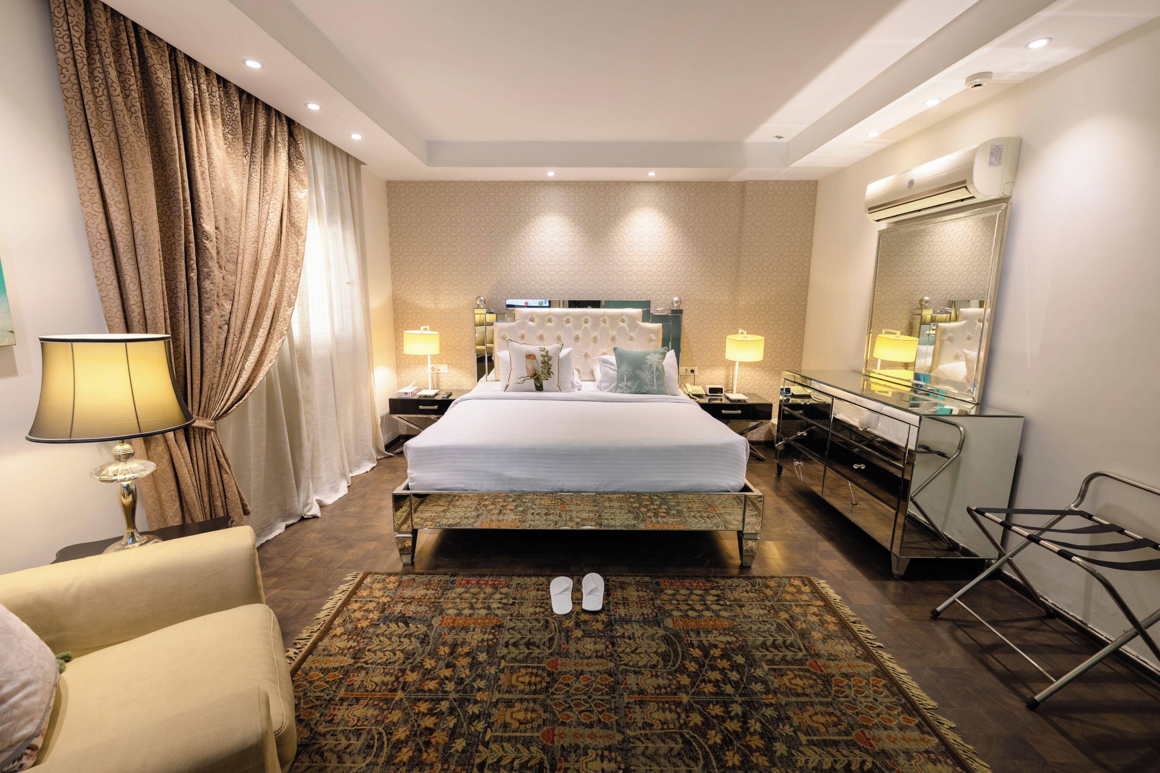 A hotel room with a bed, bedside lamps, a mirror, a desk, and a chair.