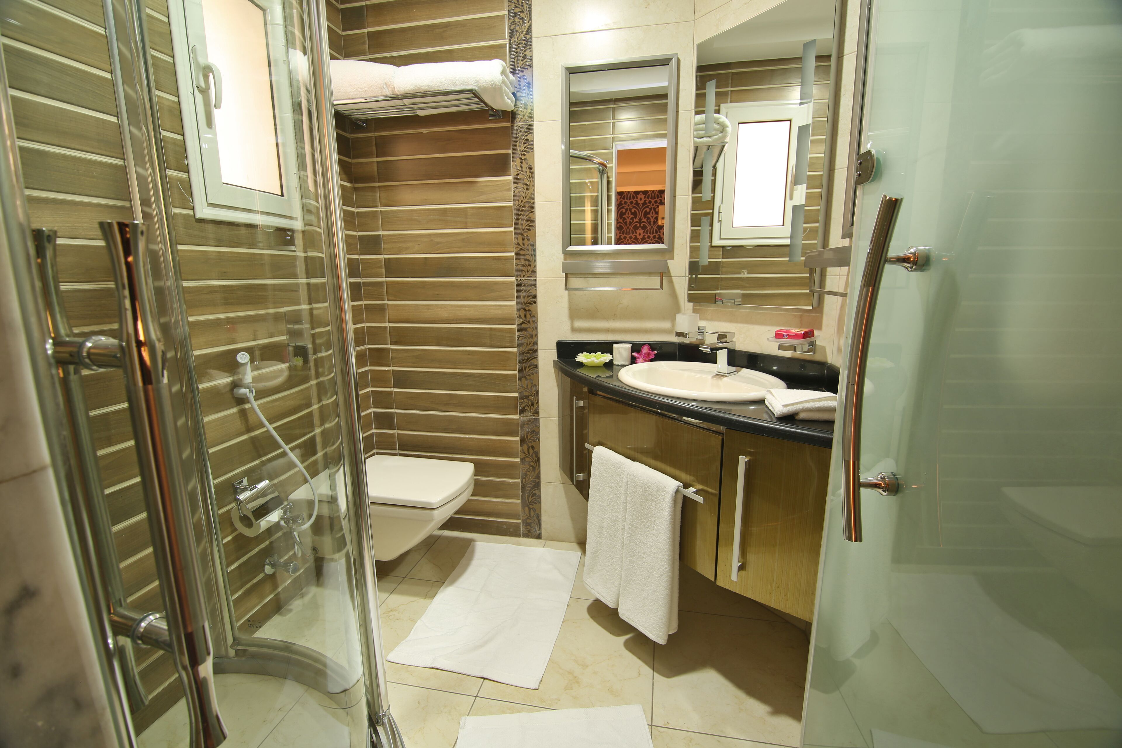 A modern bathroom with a glass shower enclosure, a toilet, a sink with a mirror, and a towel rack.