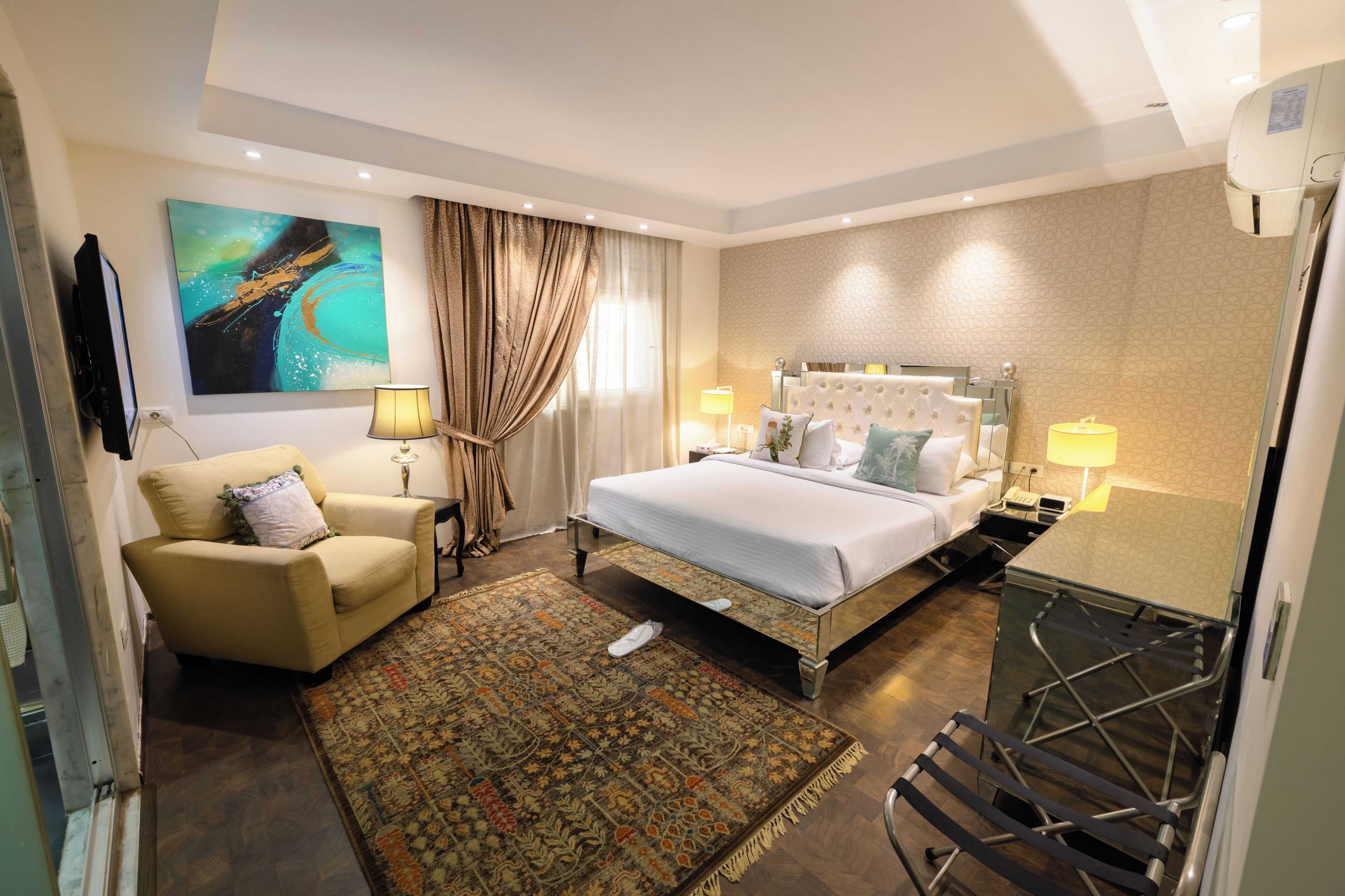 Une chambre d’hôtel avec un lit, un canapé, une télévision, un tableau, une lampe et une fenêtre avec des rideaux.