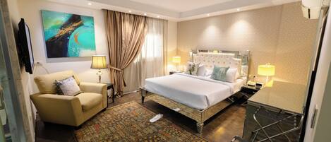 A hotel room with a bed, a sofa, a TV, a painting, a lamp, and a window with curtains.