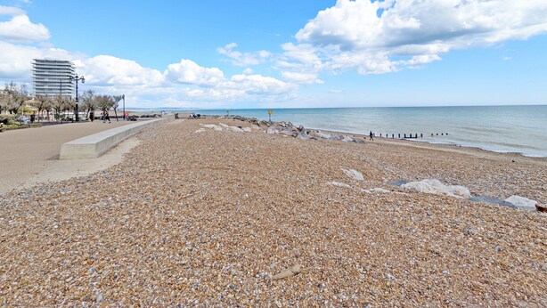 A pebbled beach with a clear sky and distant buildings.