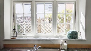 A kitchen with a window, sink, and a small shelf with bottles.