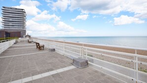 A seaside promenade with a modern building, a white fence, and a beach view.