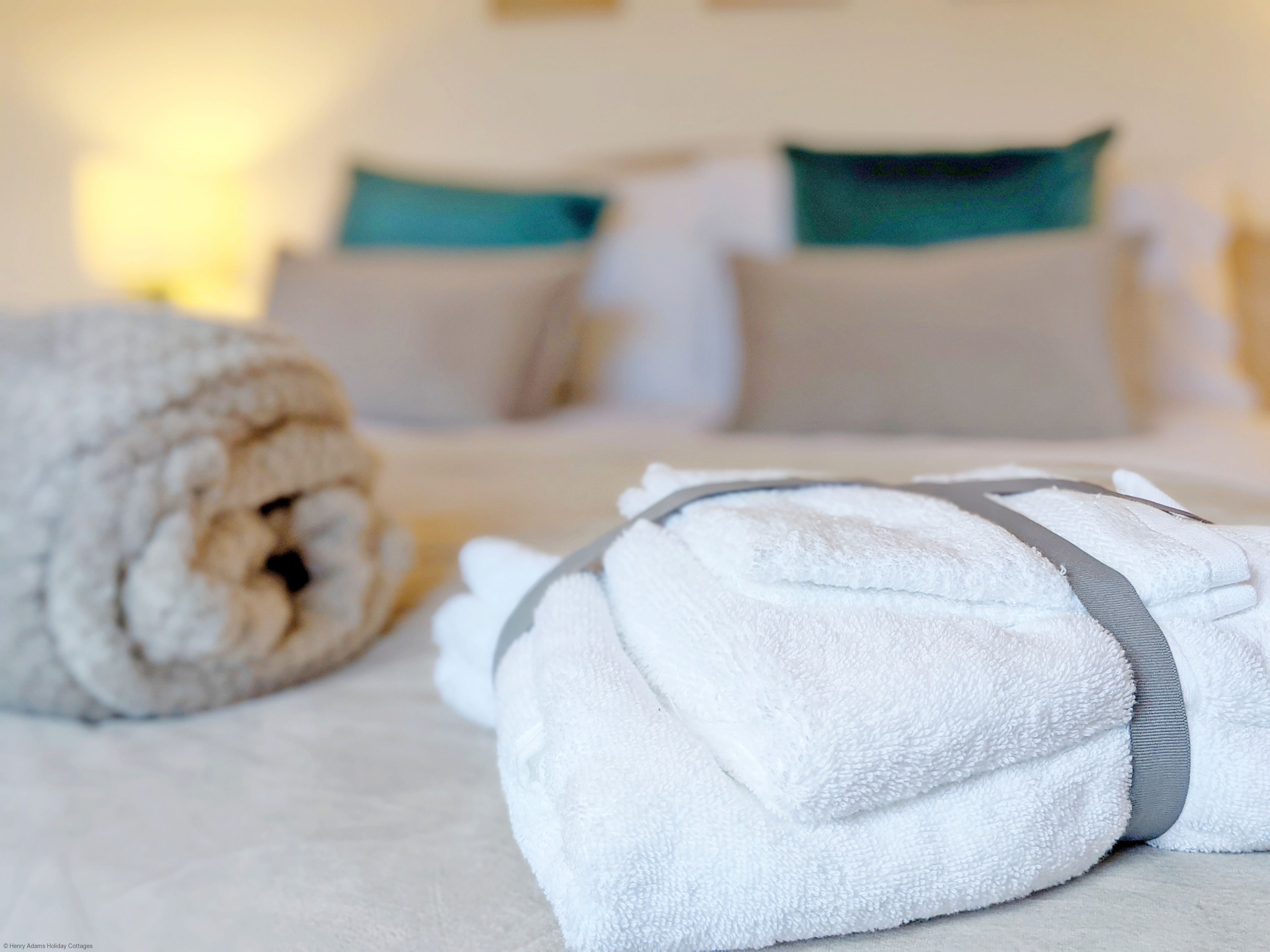 A neatly made bed with white linens and a rolled towel on the left.
