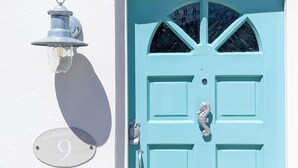 A teal door with a decorative glass window, a metal lantern, and a wooden sign reading "Seashell Cottage 9".