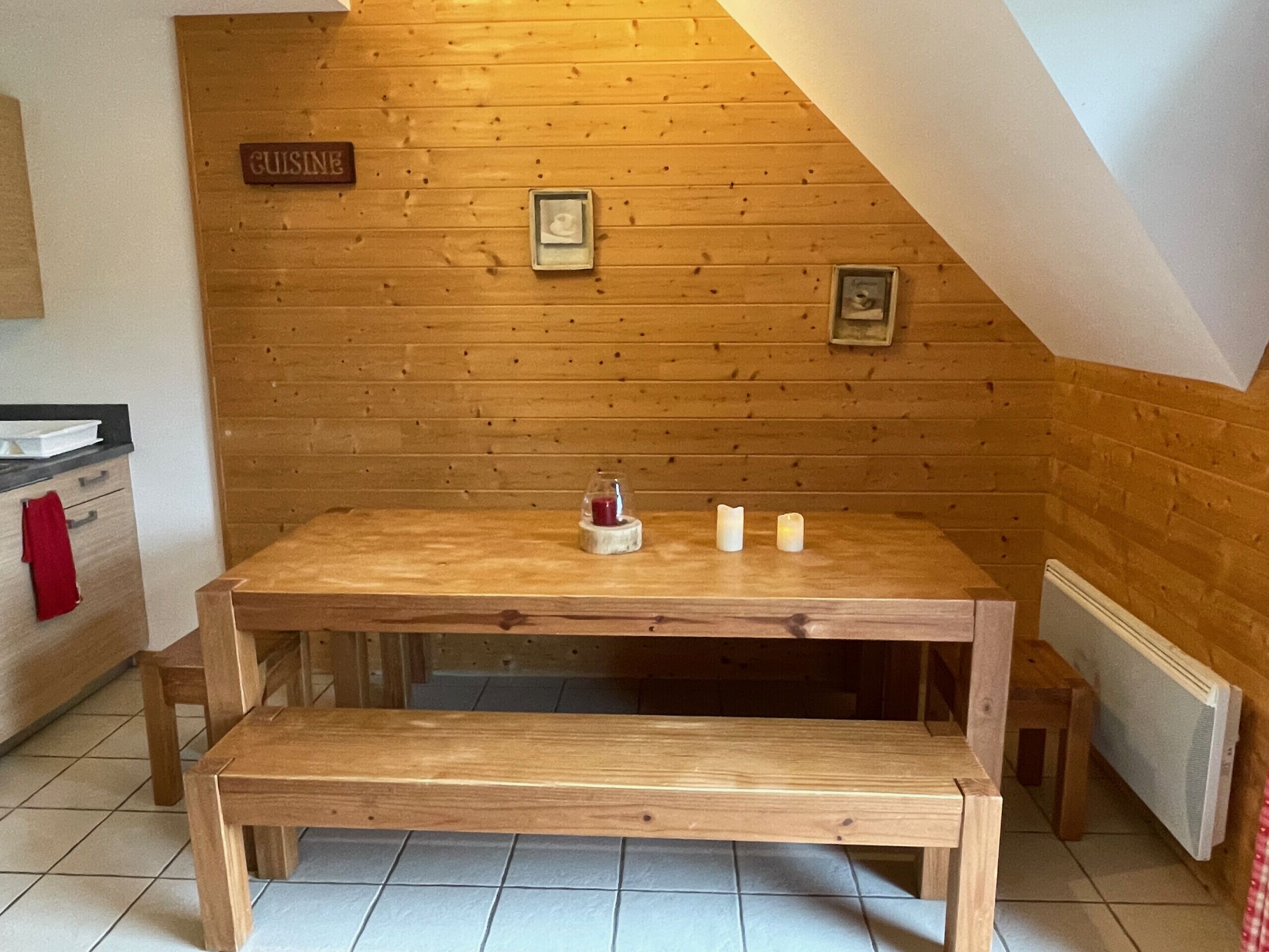 A wooden dining table with a bench, a sign reading "CUISINE", and framed pictures on the wall.