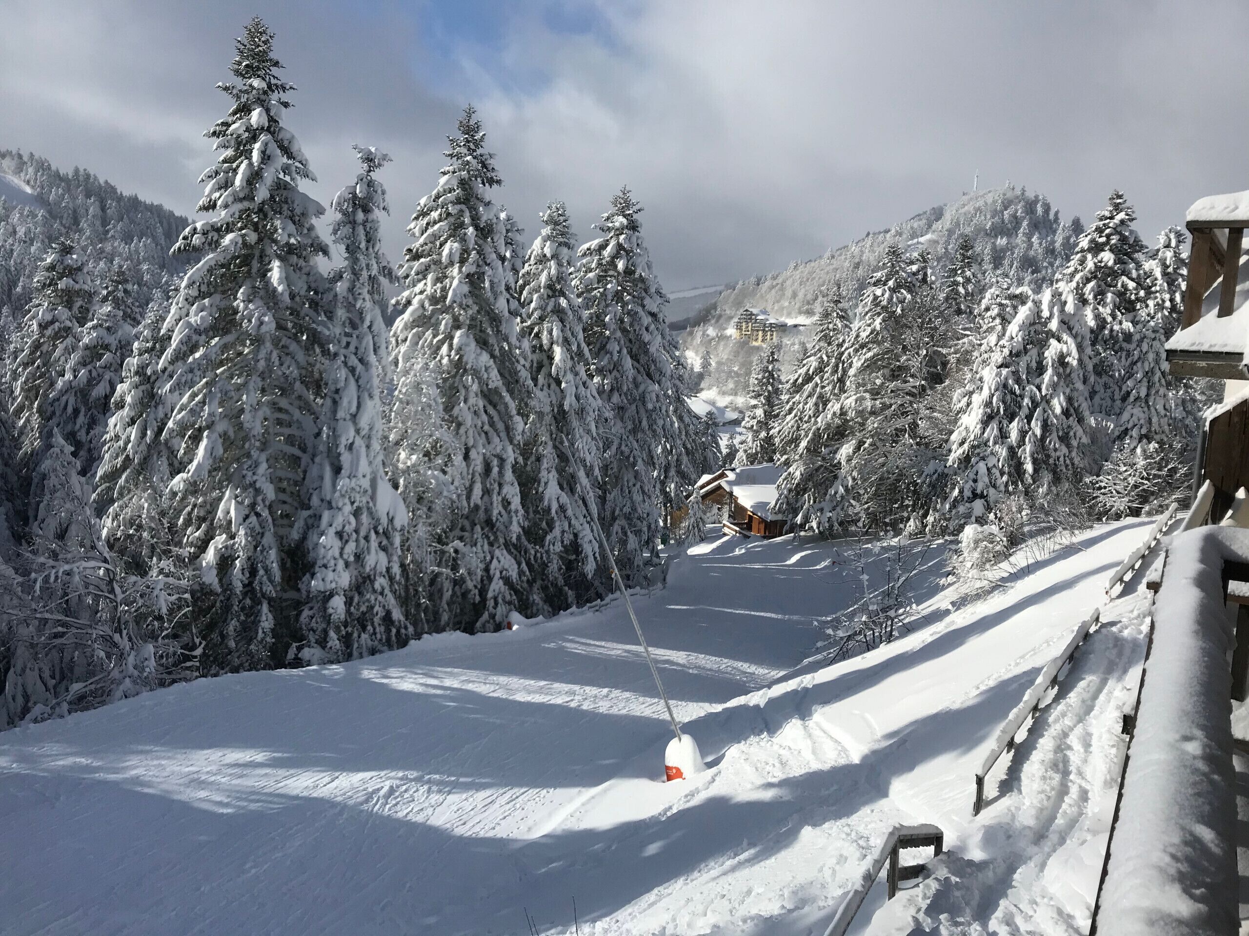 A snow-covered ski slope with a wooden cabin and trees.