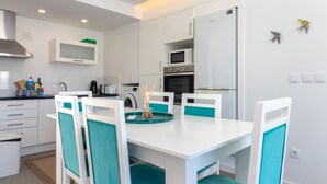 Una cocina moderna con armarios blancos, microondas, horno y un comedor con sillas blancas y azul turquesa.