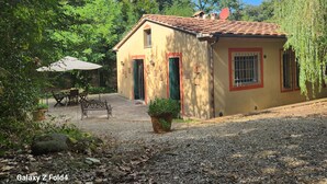 Ein kleines Haus mit Ziegeldach, einer Terrasse mit Tisch und Stühlen sowie einem Blumentopf im Vorgarten.