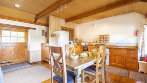 Ett lantligt kök med träskåp, ett matbord med stolar, ett kylskåp och en spis.