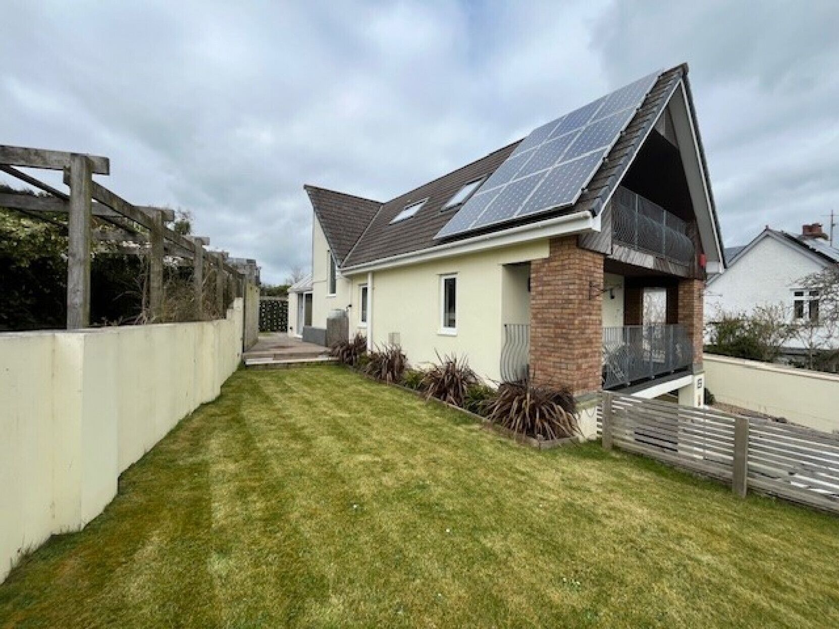 Une maison de plain-pied avec un toit en pente, des panneaux solaires, une cheminée en briques et un petit porche à l’avant.