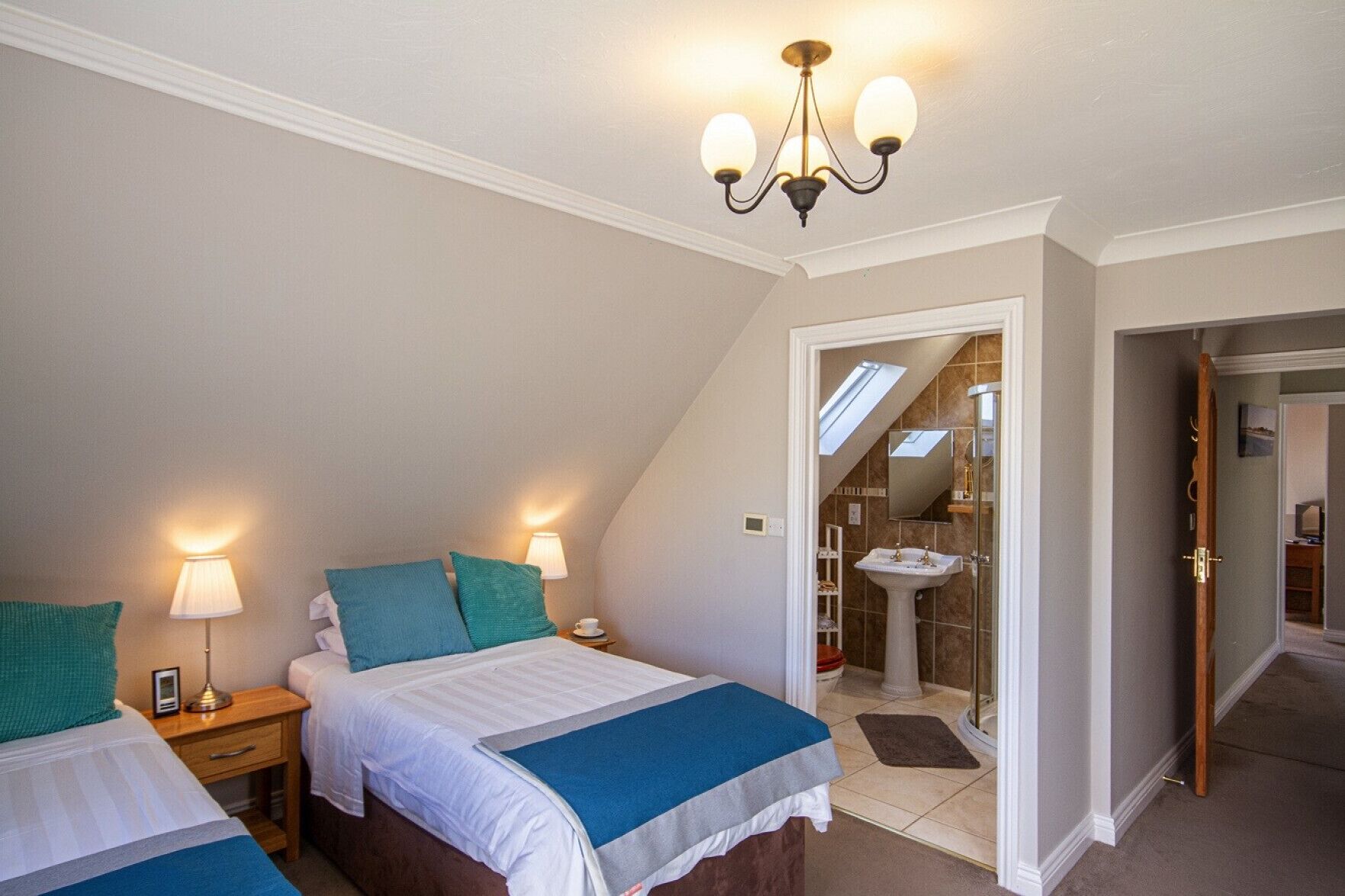 Een slaapkamer met twee bedden, een kroonluchter, een badkamer met een wastafel en spiegel, en een dakvenster.