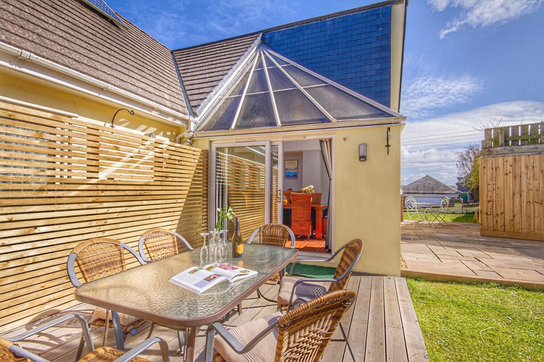 A patio with a glass-top table, wicker chairs, and a small glass-enclosed dining area.