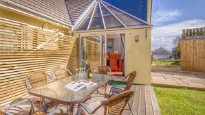 Eine Terrasse mit einem Glastisch, Korbstühlen und einem kleinen, verglasten Essbereich.