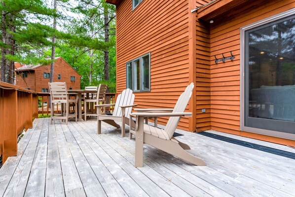 Puinen terassi, jossa on Adirondack-tyyliset tuolit ja pöytä, ja jonka ympärillä on puinen aita ja puita.