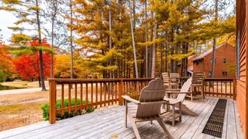 A wooden deck with outdoor seating, surrounded by trees with autumn foliage.