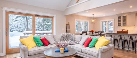A modern living room with a sectional sofa, a round coffee table, and a view of a snowy landscape through large windows.
