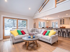 A modern living room with a sectional sofa, a round coffee table, and a view of a snowy landscape through large windows. - Colorful Oasis: Modern, Water View, Family-Friendly (Conway)