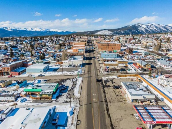 An aerial view of a town with a main road, buildings, and snow-covered mountains in the background.
