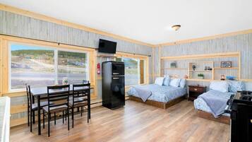 A compact room with a dining table, two beds, a TV, and a refrigerator.