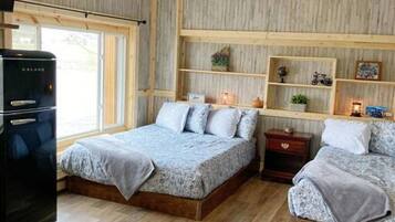A bedroom with two beds, wooden flooring, a built-in shelf unit, and a refrigerator.
