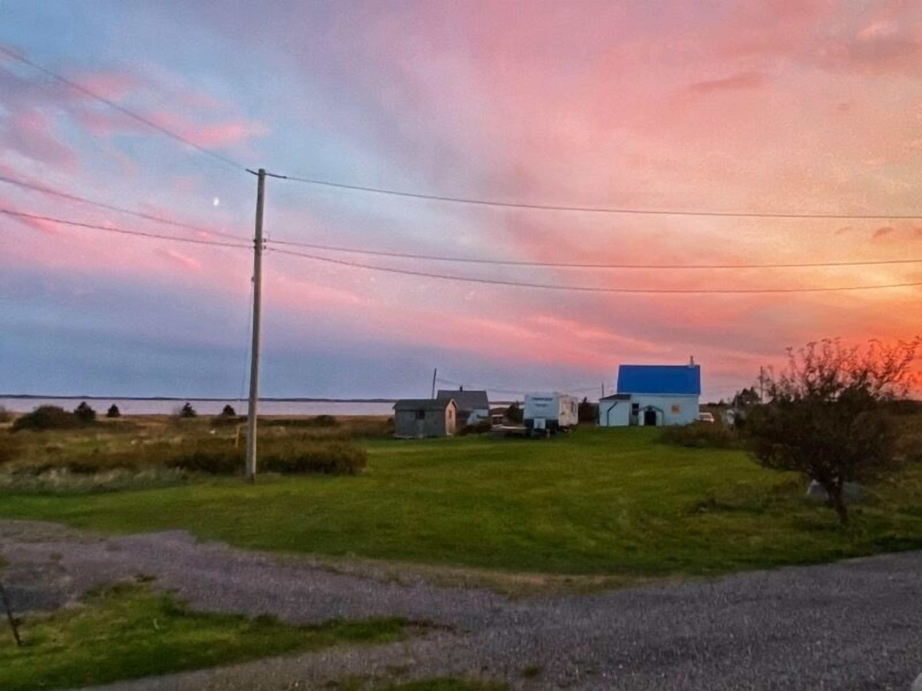 Ländliche Landschaft mit einem Haus und einer Scheune, umgeben von offenen Feldern und wolkenlosem Himmel.