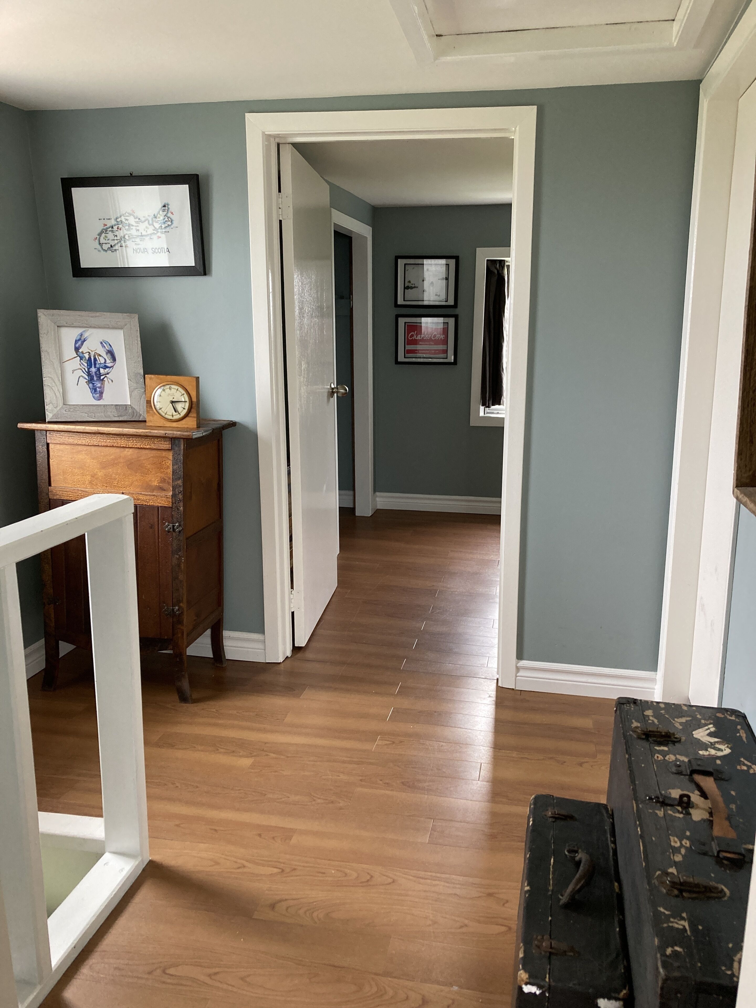 A hallway with wooden flooring, a vintage clock, and framed artwork on the wall.