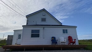 A two-story white house with a wooden deck, a small window, and a door. - Seaside Cottage in Beautiful Charlo’s Cove (Charlo's Cove)