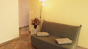 Quarto com sofá verde, duas almofadas, abajur e um vaso com flores.