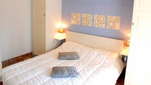 Quarto com uma cama, duas luminárias de cabeceira, cabeceira com painel decorativo e uma porta à esquerda.