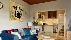 A modern living room with a blue sofa, a round wooden coffee table, and a kitchen in the background. - 1 Bed Flat - Sleeps 5 - Parking - Garden - Pets (Larne)