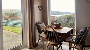 A dining area with a table and chairs, a view of the outdoors, and a window with curtains. - 1 Bed Flat - Sleeps 5 - Parking - Garden - Pets (Larne)