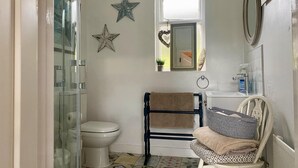 A bathroom with a glass shower enclosure, a toilet, a sink with a mirror, and a chair with towels. - 1 Bed Flat - Sleeps 5 - Parking - Garden - Pets (Larne)