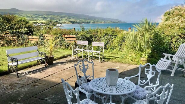 A patio with white metal furniture, a bench, and a view of a coastal landscape. - 1 Bed Flat - Sleeps 5 - Parking - Garden - Pets (Larne)
