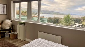 A bedroom with a large window, a bed, a chair, a radiator, and a radiator cover. - 1 Bed Flat - Sleeps 5 - Parking - Garden - Pets (Larne)