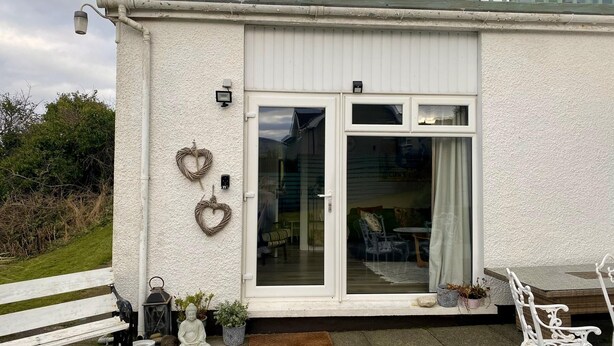 A white building with a glass door and windows, a bench, a statue, and heart-shaped decorations. - 1 Bed Flat - Sleeps 5 - Parking - Garden - Pets (Larne)