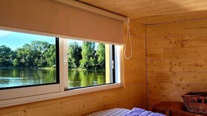 Mökki, jossa on sänky, ikkuna, josta avautuu näkymä järvelle, ja puuseinät.