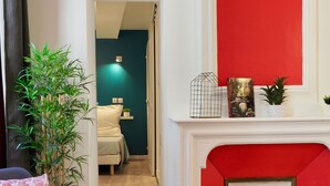 Ein modernes Wohnzimmer mit roter Akzentwand, einem Kamin, einem blauen Sessel, Holzboden und einer Treppe zu einem anderen Raum.
